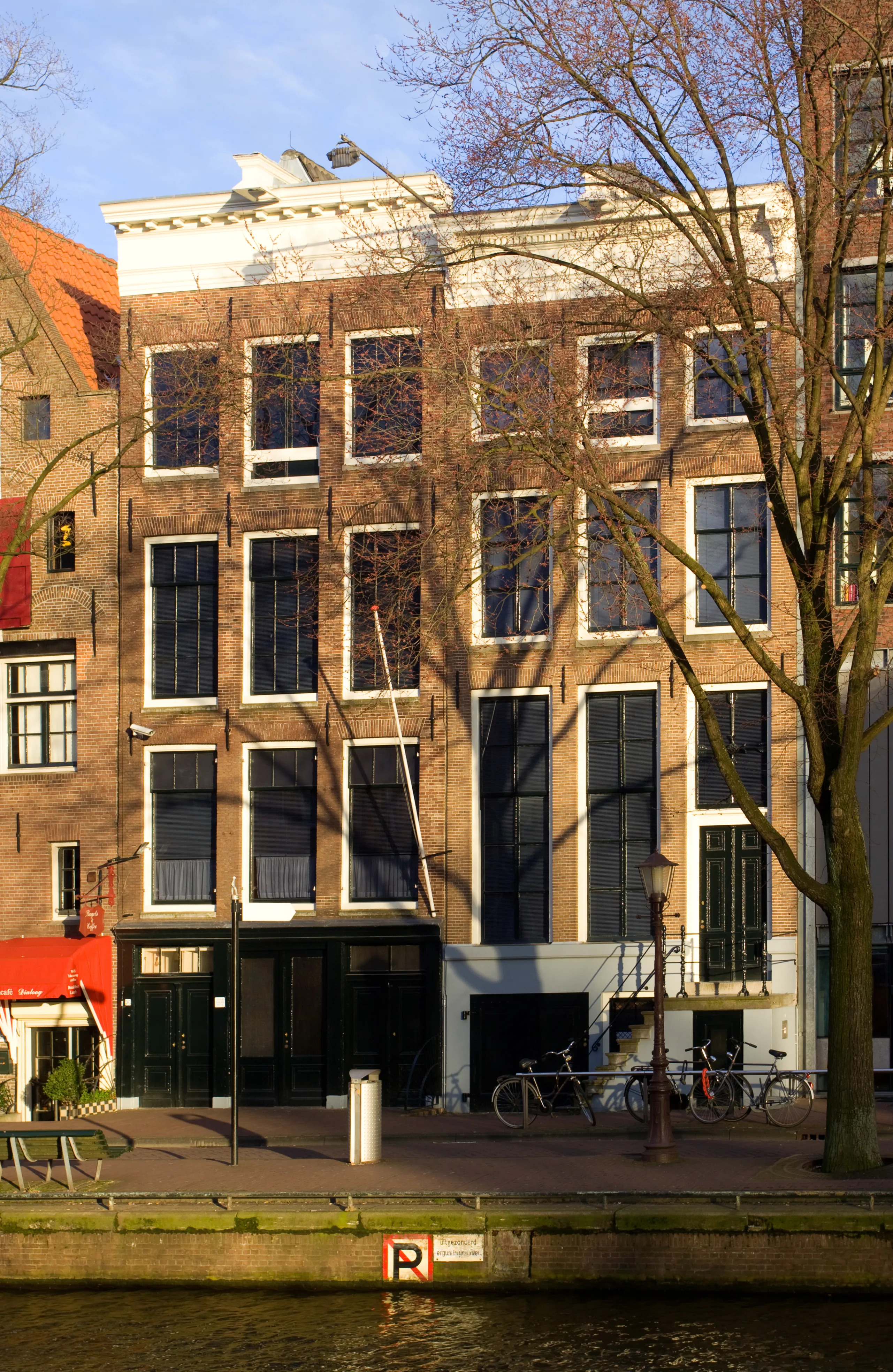 Een oranjegekleurde menigte op de Amsterdamse grachten tijdens Koningsdag met versierde bootjes op het water