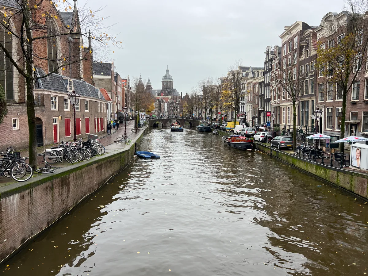 Het Oudezijds Voorburgwal-kanaal in De Wallen in Amsterdam met historische gevels en de Oude Kerk op de achtergrond